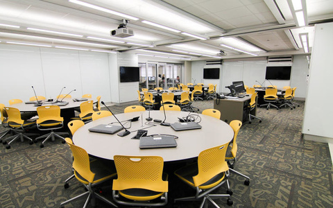 Image of empty classroom with round tables and yellow chairs