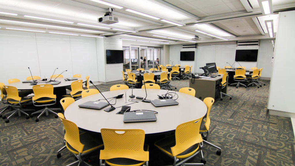 Image of empty classroom with round tables and yellow chairs