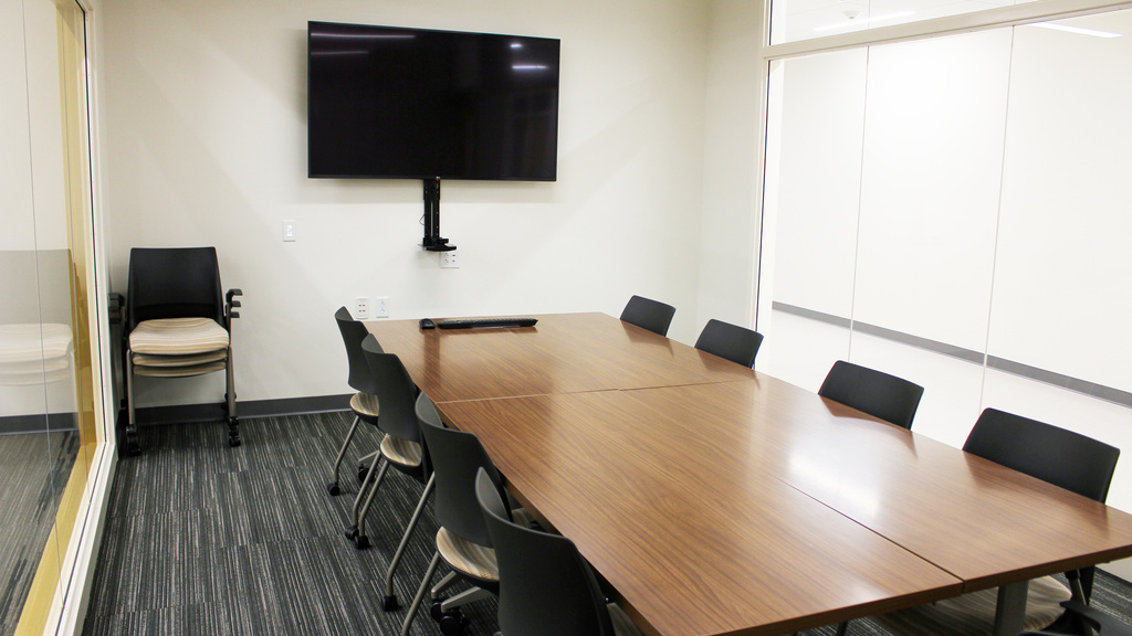 Image of small room with conference table surrounded by chairs and monitor on wall
