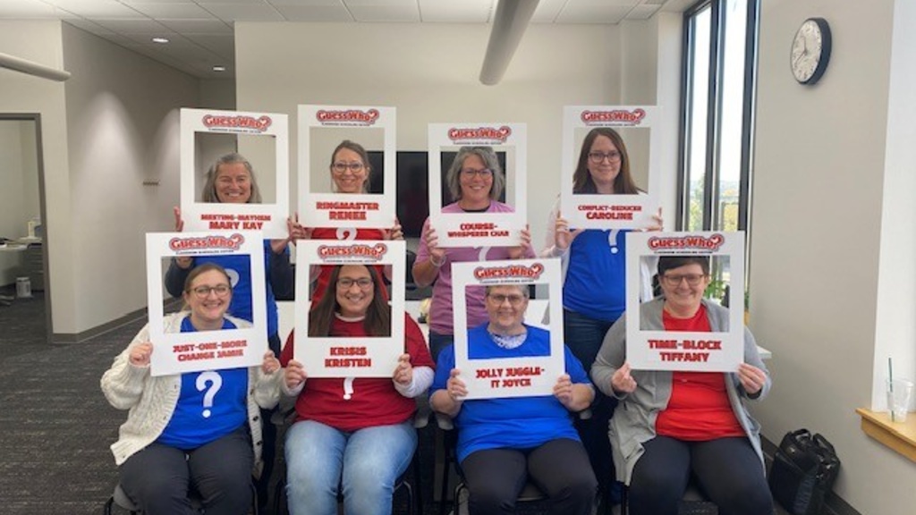 group of eight women holding signs that portray them as characters from the game Guess Who